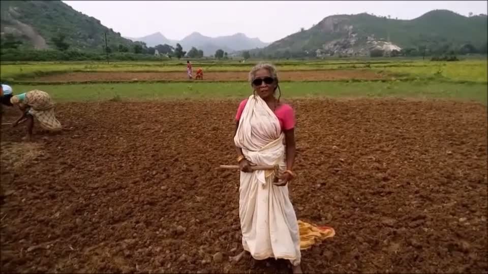 Still from Eka Nari Sangathan &mdash; a woman in a white sari stands in a ploughed field below green hills