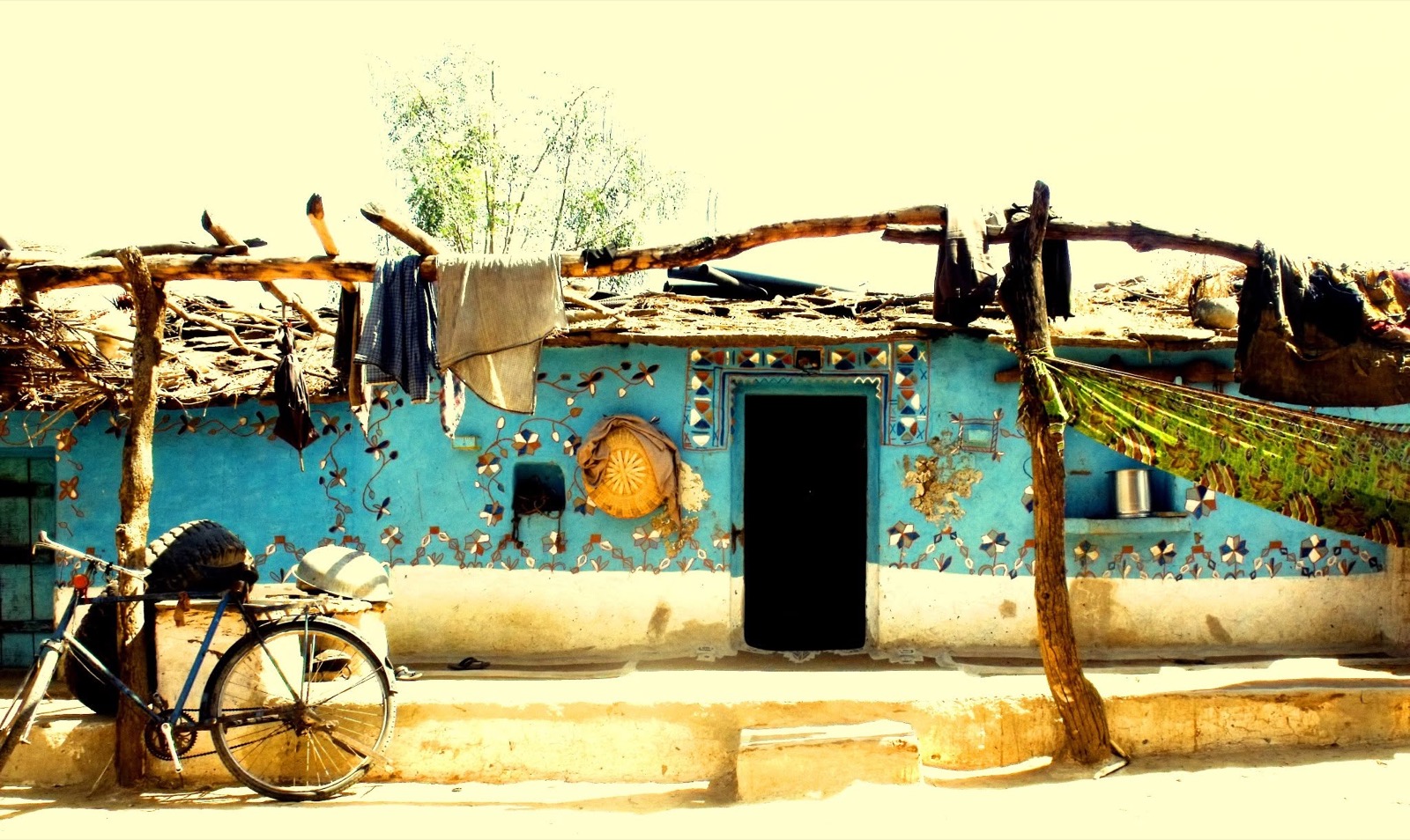 A blue-painted village house decorated with small mirrors, a bicycle leaning against its low wall