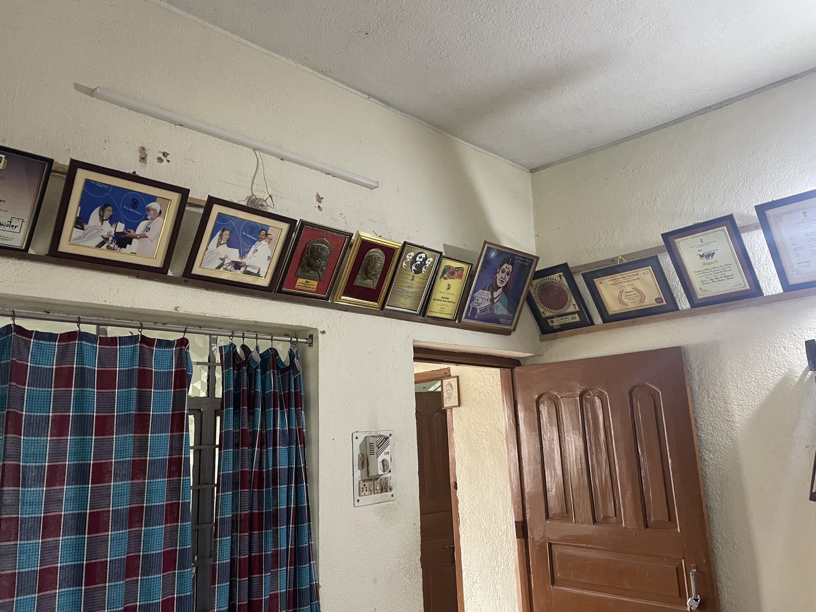 A row of framed awards and photographs running along the top of an office wall above a checked curtain
