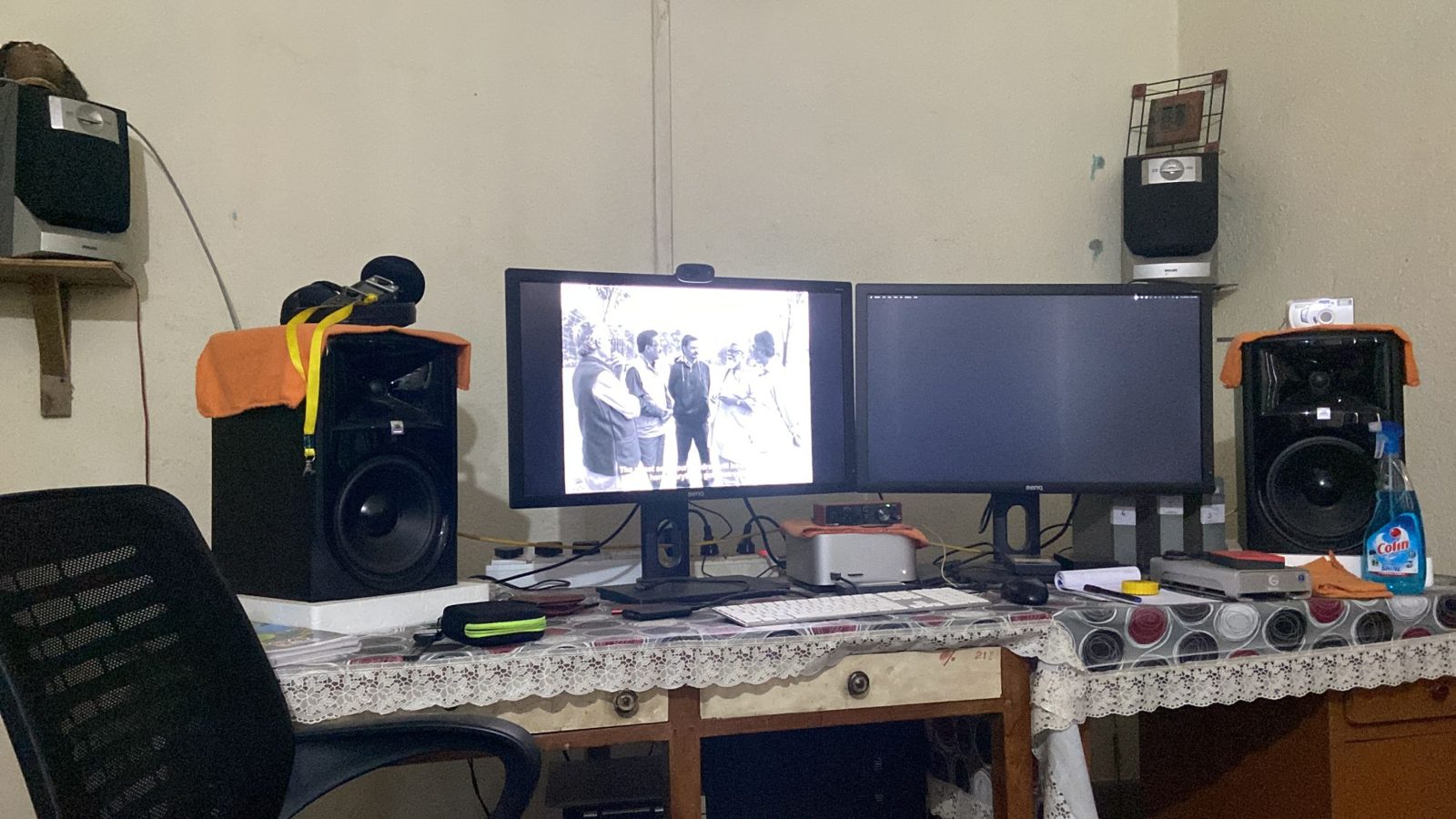 The same editing desk at night, one monitor showing a black-and-white frame of five men talking outdoors, with subtitles